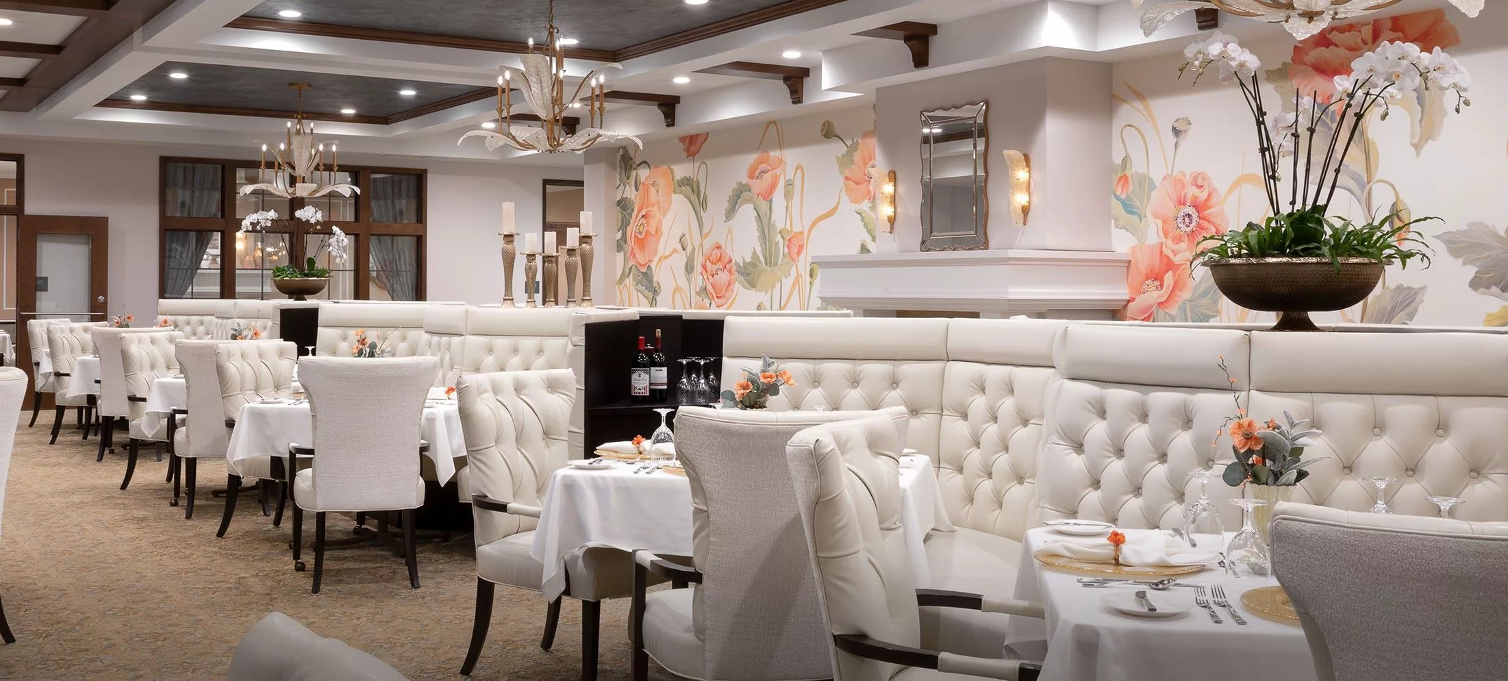 An elegantly decorated restaurant with white upholstered seating and chandeliers, featuring a sophisticated dining atmosphere.