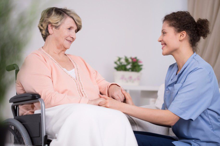 A nurse providing care and support to an elderly woman in a wheelchair.