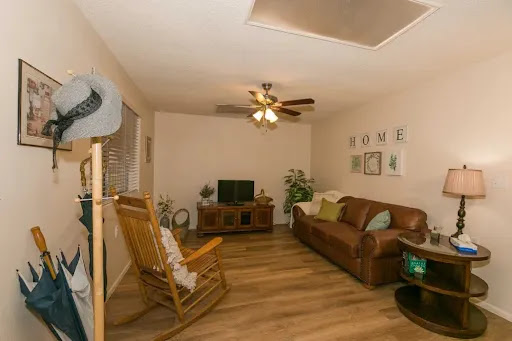 A cozy living room featuring a comfortable couch, a rocking chair, and a television, set against warm wooden flooring.