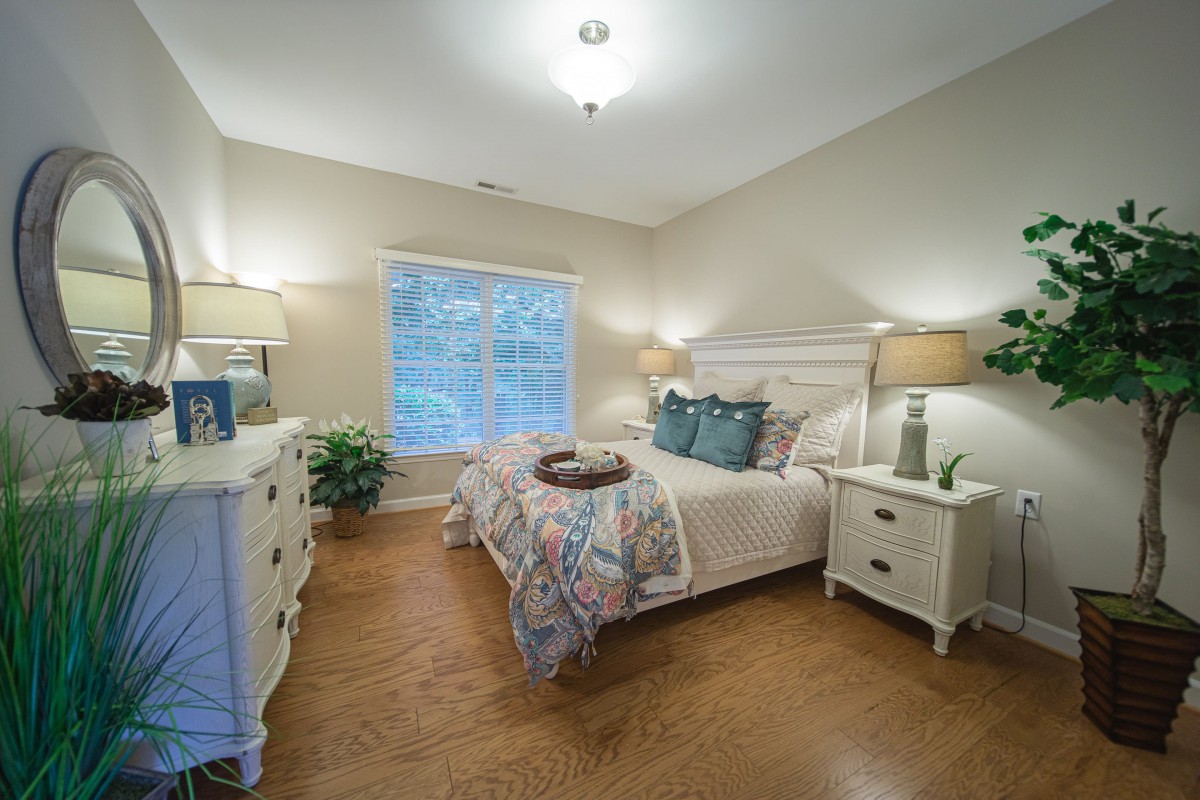 A cozy bedroom with a neatly made bed, wooden floors, and elegant decor.