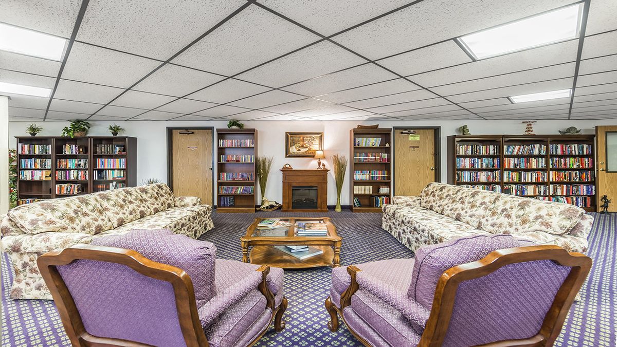 A cozy living room with patterned sofas, armchairs, bookshelves, and a fireplace.