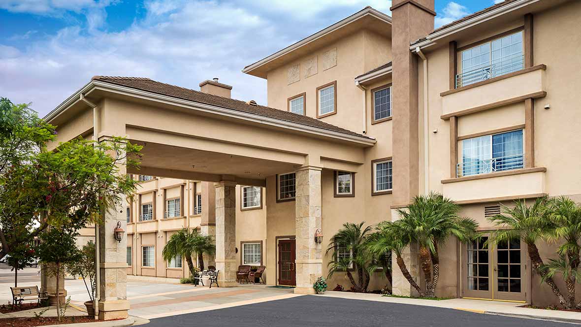 A modern hotel exterior with a covered entrance and palm trees.