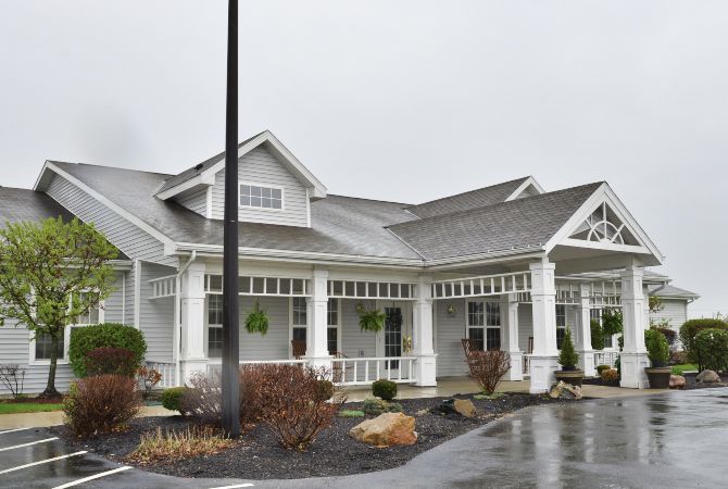 A white building with a porch and gabled roof on a rainy day.