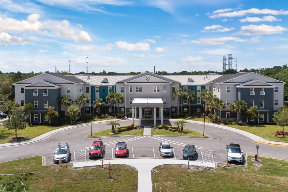 A large apartment complex with a central entrance and adjacent parking area on a sunny day.