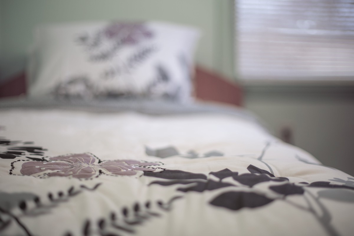 A neatly made bed with a patterned comforter and pillow in a softly lit room.