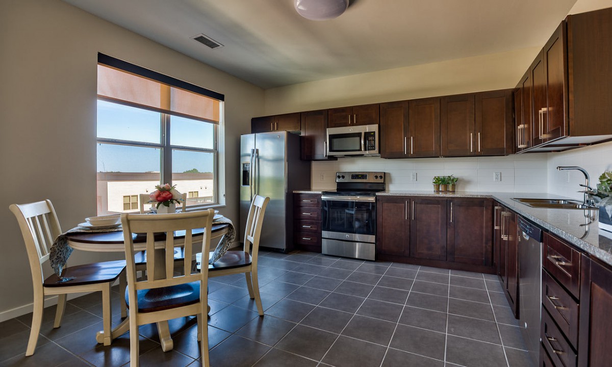 A modern kitchen with stainless steel appliances and a cozy dining area, bathed in natural sunlight.