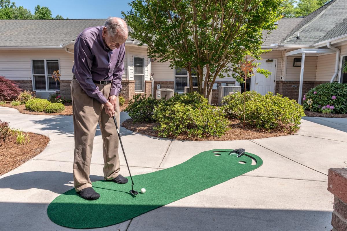 An elderly man enjoys a game of mini-golf on an outdoor putting green in a residential area.