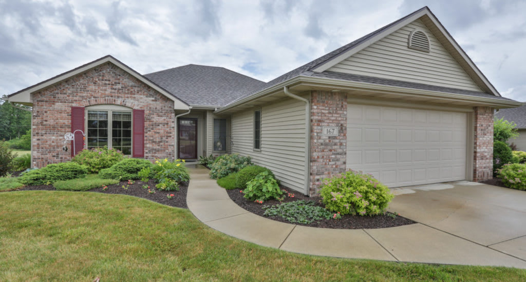 A suburban house with brick and siding exterior, surrounded by a well-maintained lawn and landscaped walkway.