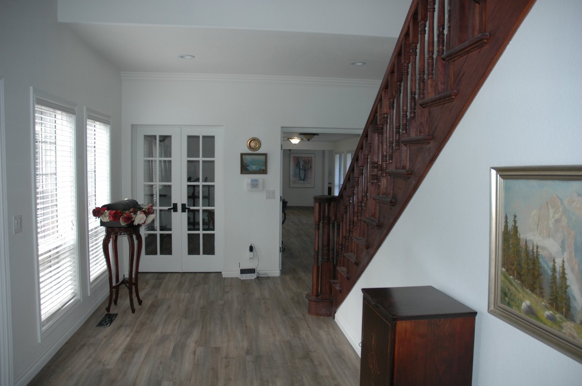 A hallway with wooden stairs, French doors, and a table with a vase.
