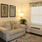 Cozy living room with a comfortable sofa, decorative cushions, wall art, and a lamp beside the window.