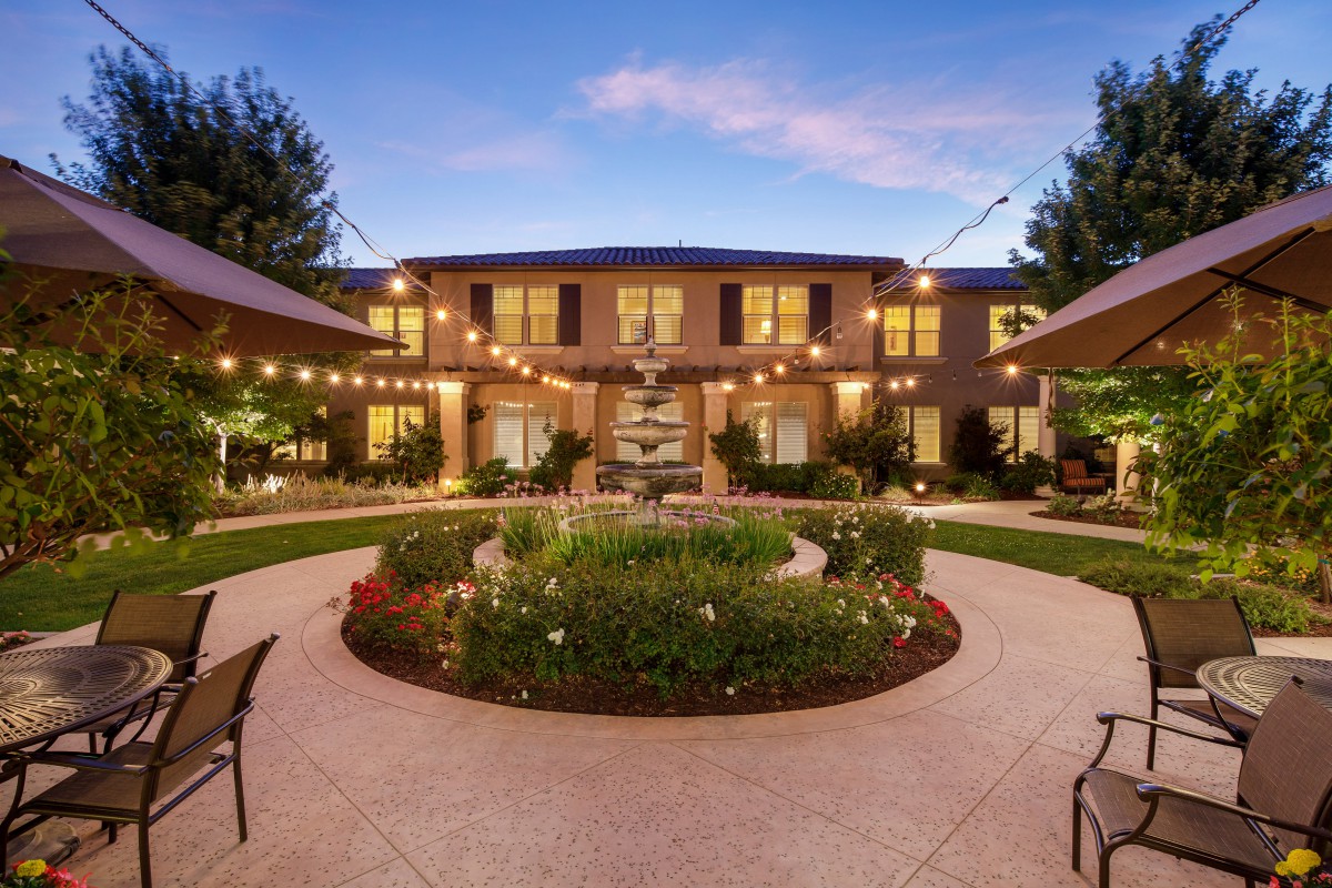 A beautifully landscaped garden with pathways and string lights leads to a two-story house at dusk.