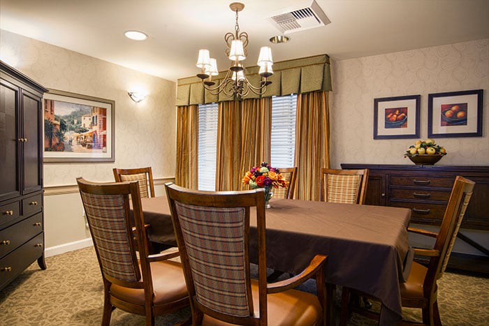 A cozy dining room with a table and chairs, illuminated by a chandelier and natural light through the curtains.