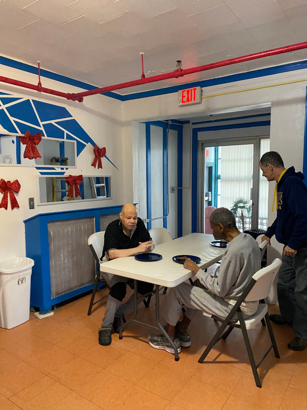 Three people interacting around a dining table in a community setting.