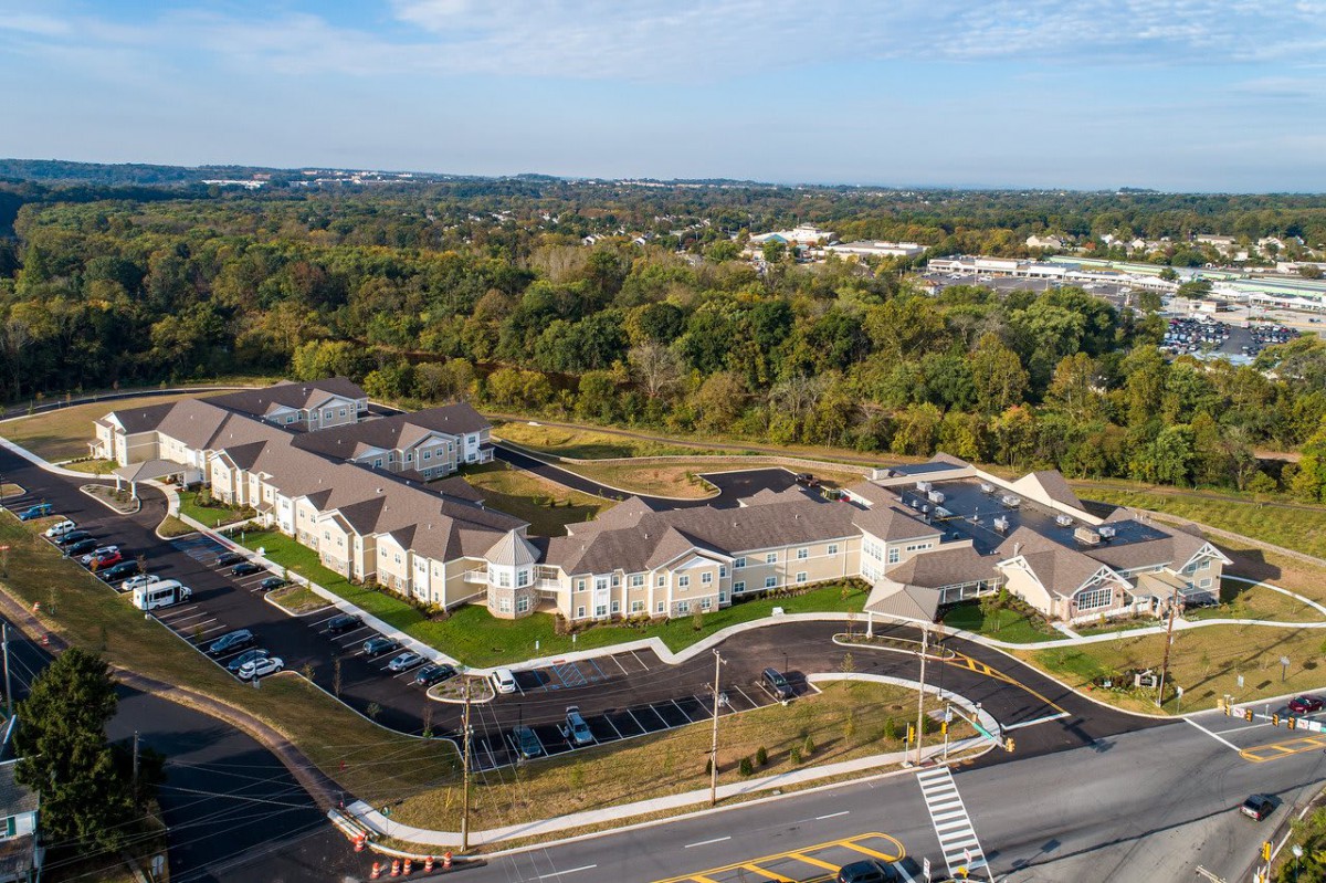 Aerial view of a suburban residential complex with surrounding greenery and a road intersection.