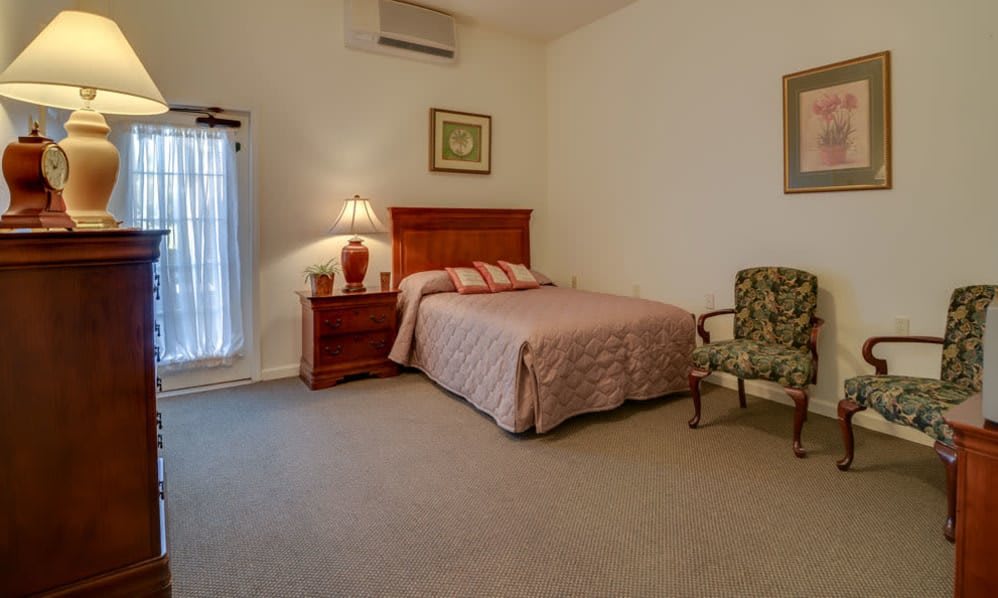 A cozy bedroom with a neatly made bed, nightstand, and comfortable chair.