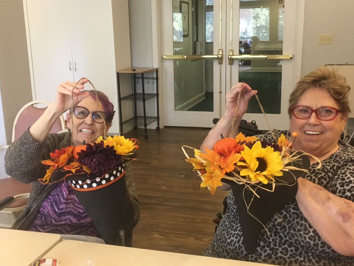 Two seniors happily display their colorful flower arrangements during a crafting session.