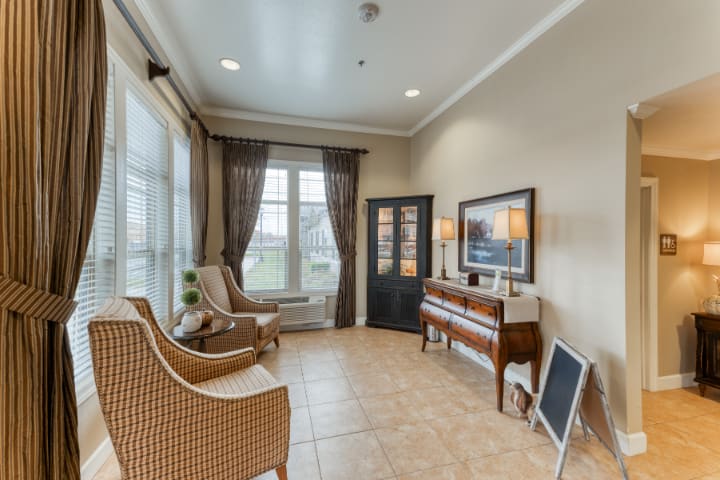 A cozy living room featuring a piano, wicker chairs, and large windows with curtains.