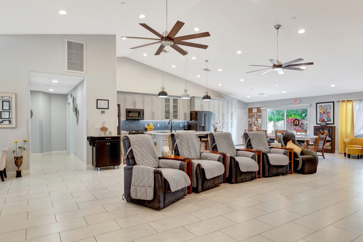 A spacious modern living area featuring multiple recliners, a kitchen in the background, and ceiling fans.