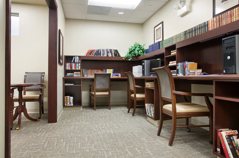 A quiet office space featuring several desks and chairs, surrounded by bookshelves filled with books.