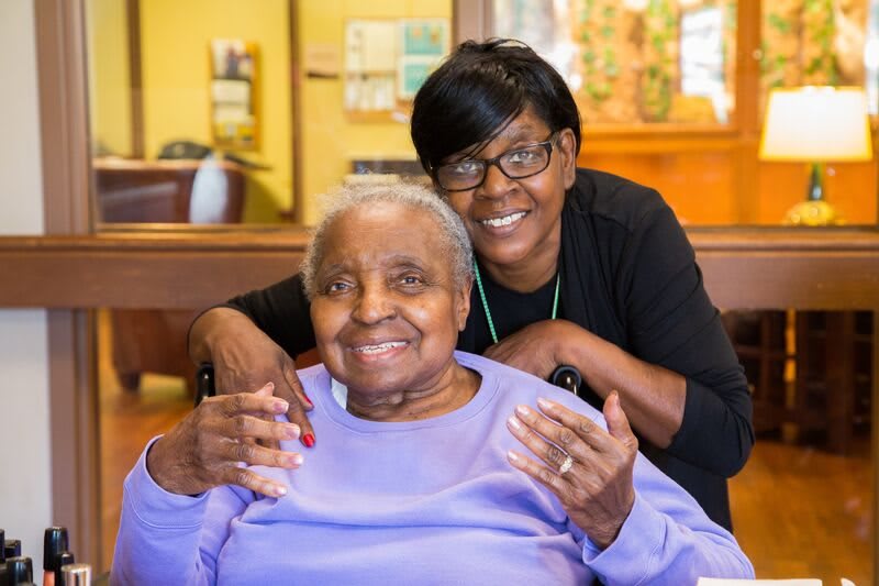 A caregiver smiles alongside an elderly woman, showing companionship and care.
