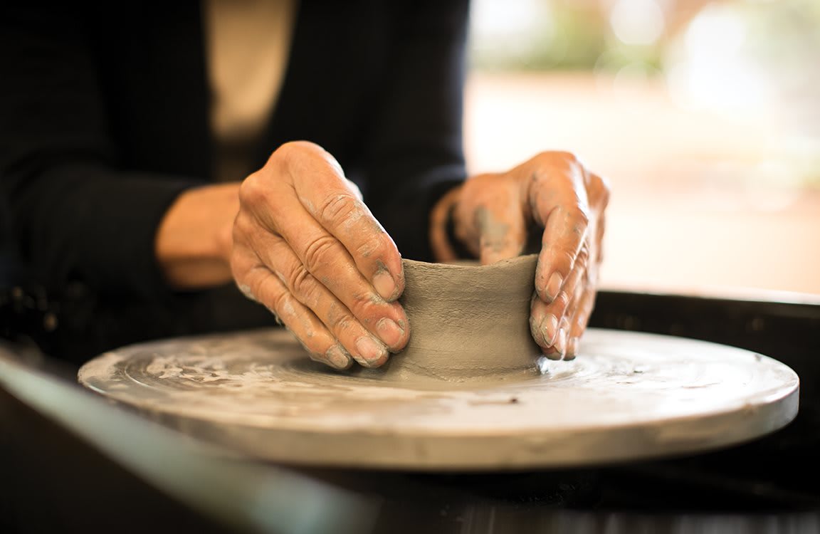 Hands shaping clay on a pottery wheel.