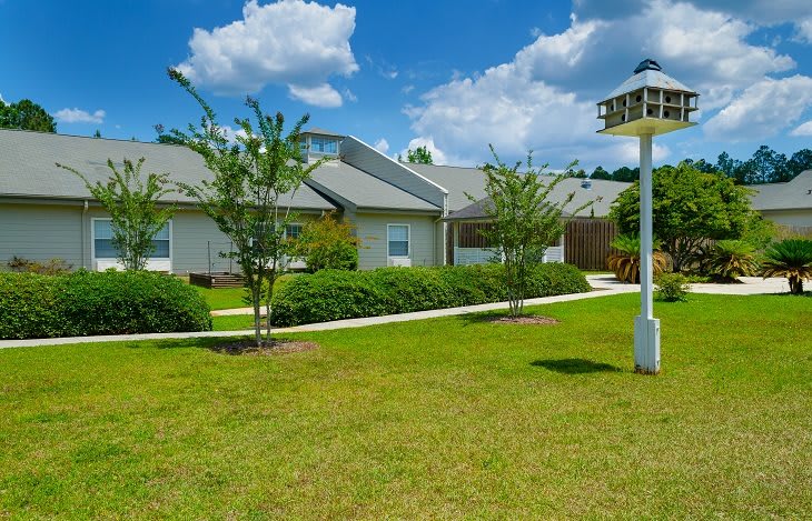 A charming residential property with a well-maintained lawn, garden, and birdhouse under a clear blue sky.