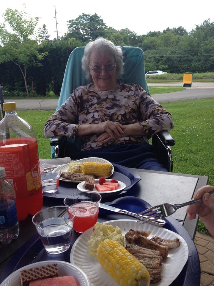 An elderly person enjoying a picnic outdoors with various foods and drinks on the table.