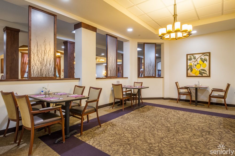 A cozy restaurant dining area featuring elegant interior design with tables and chairs, accented by a chandelier and carpeted flooring.