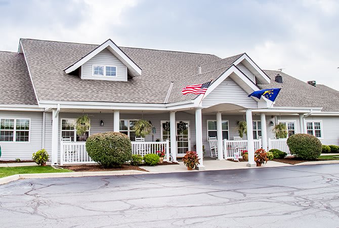 A well-maintained building with a porch, displaying two flags and surrounded by neatly arranged landscaping.
