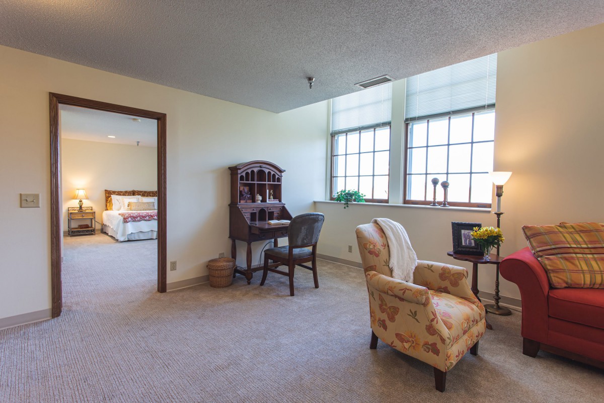 A cozy living room area with a desk, armchair, and large windows.