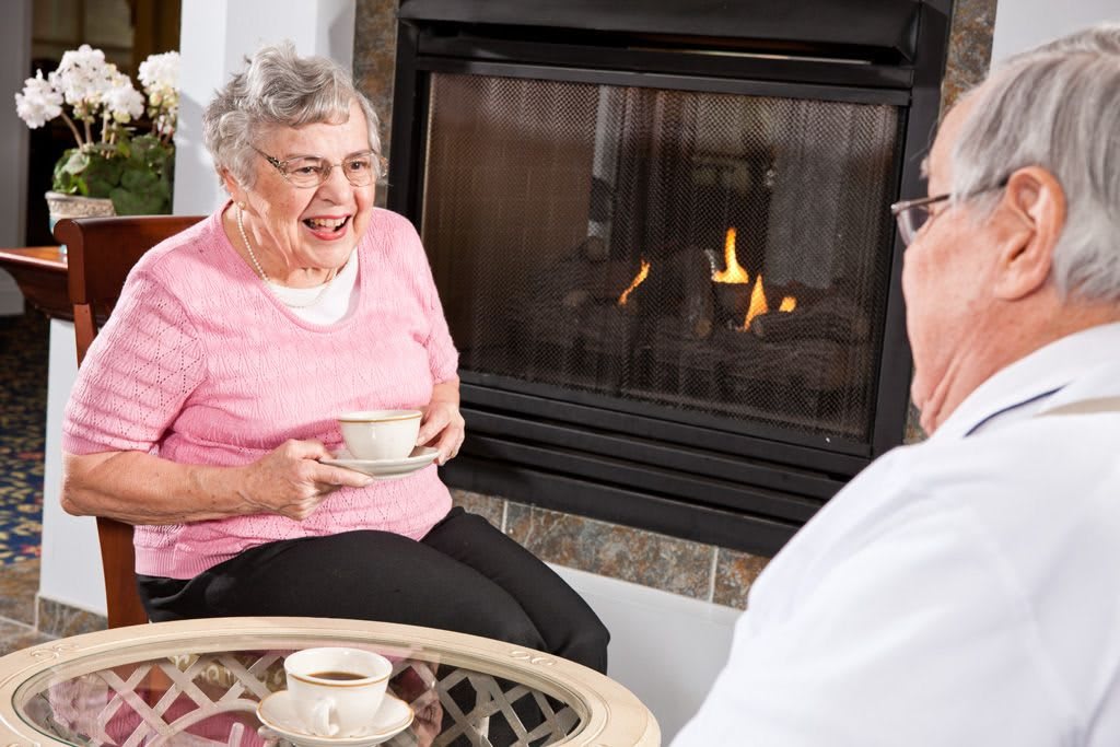 Elderly couple enjoying coffee by the fireplace.