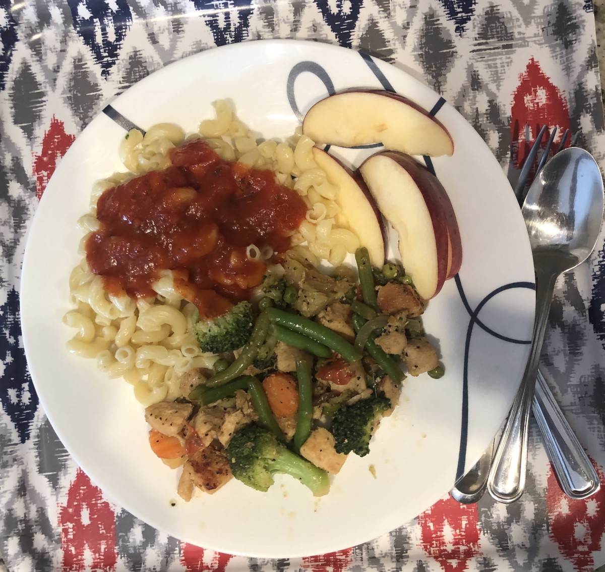 A plate featuring pasta with sauce, sauted vegetables, and apple slices.