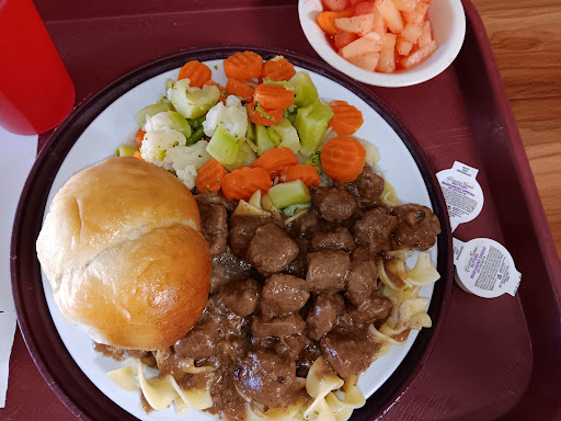 A hearty lunch plate featuring beef stew served over noodles, accompanied by mixed vegetables and a fresh fruit salad.