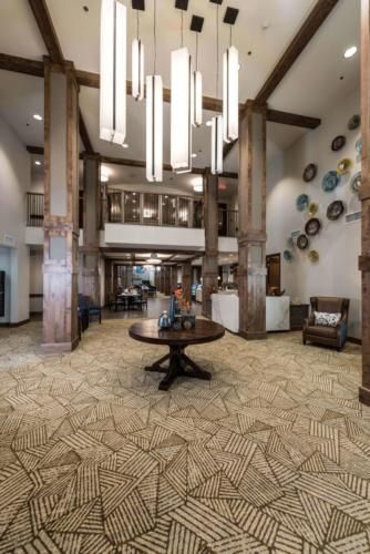 A spacious and elegantly designed hotel lobby featuring modern decor, large chandeliers, and wooden beams.