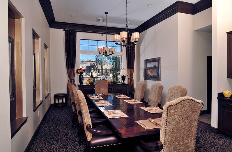 A luxurious dining room with a long wooden table, upholstered chairs, and a chandelier hanging from the ceiling.