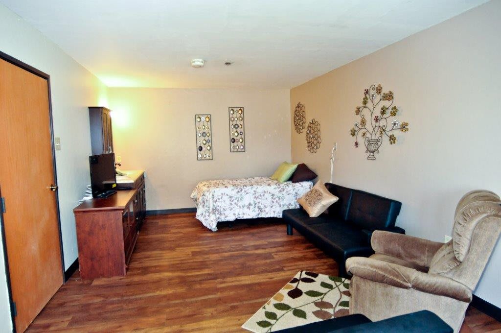 A cozy studio apartment featuring a bed, sofa, and wooden flooring with decorative wall art.