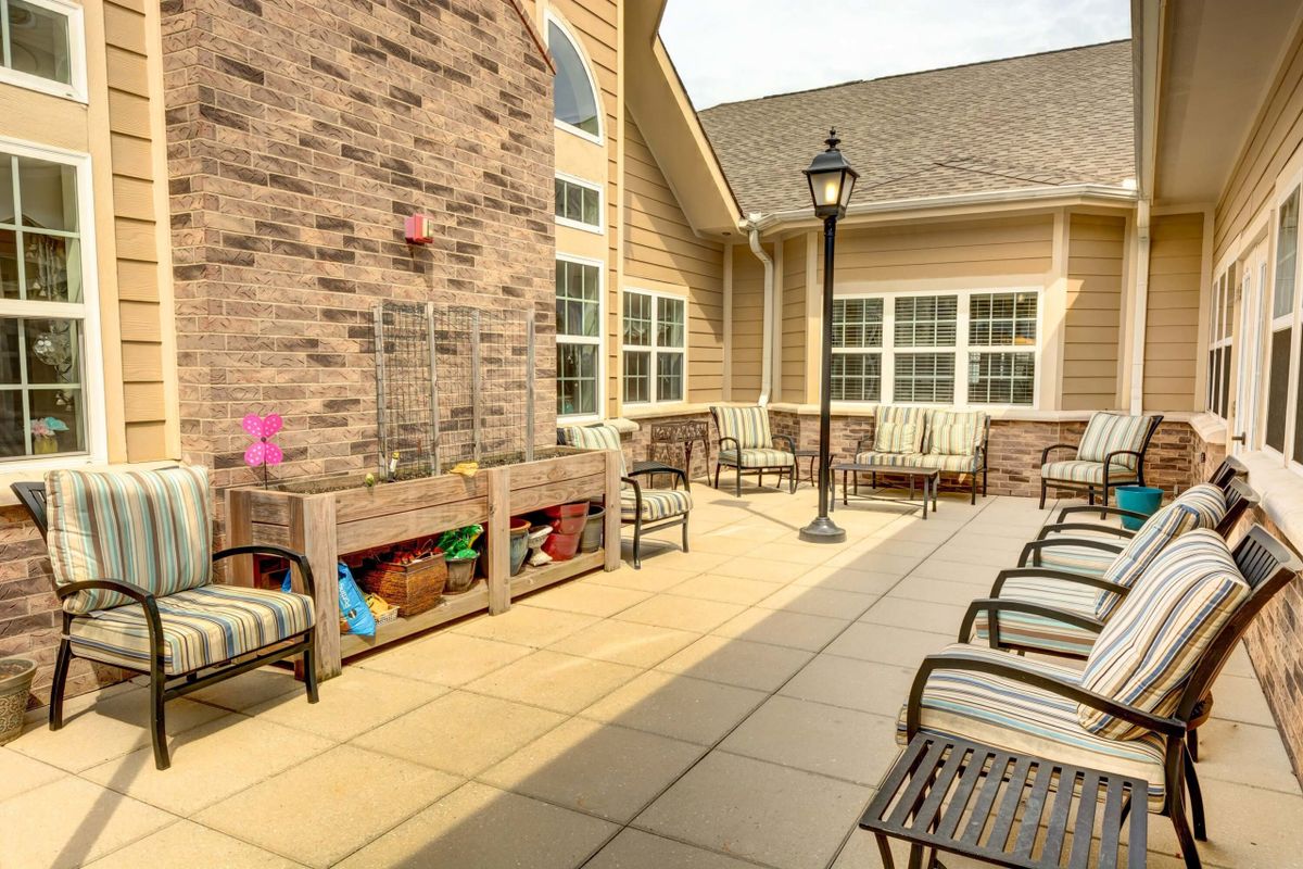 A well-furnished patio area with chairs and a bench, surrounded by a brick wall and large windows.