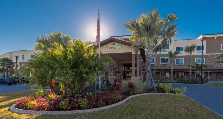A well-landscaped building entrance with palm trees and a flag under a clear blue sky.