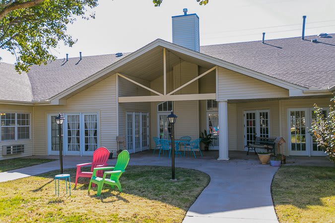 A backyard view of a house with a patio and colorful chairs on the lawn.