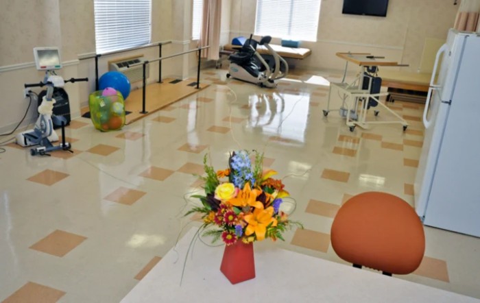 A rehabilitation center room with exercise equipment and a floral arrangement on a table.