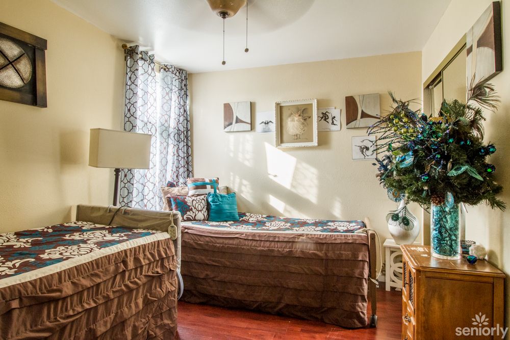 A cozy and well-decorated bedroom featuring two beds, patterned curtains, decorative pillows, framed wall art, and a touch of natural light.
