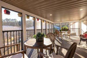 A cozy enclosed porch with wooden furniture and plants, basking in natural light.