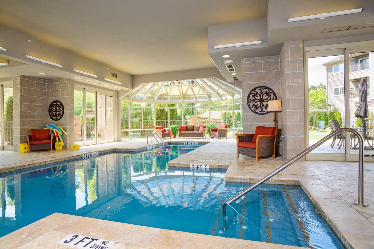 A luxurious indoor swimming pool with modern furniture and large glass walls offering outdoor views.