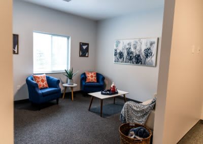 A cozy living room with blue chairs, a window, and wall art.