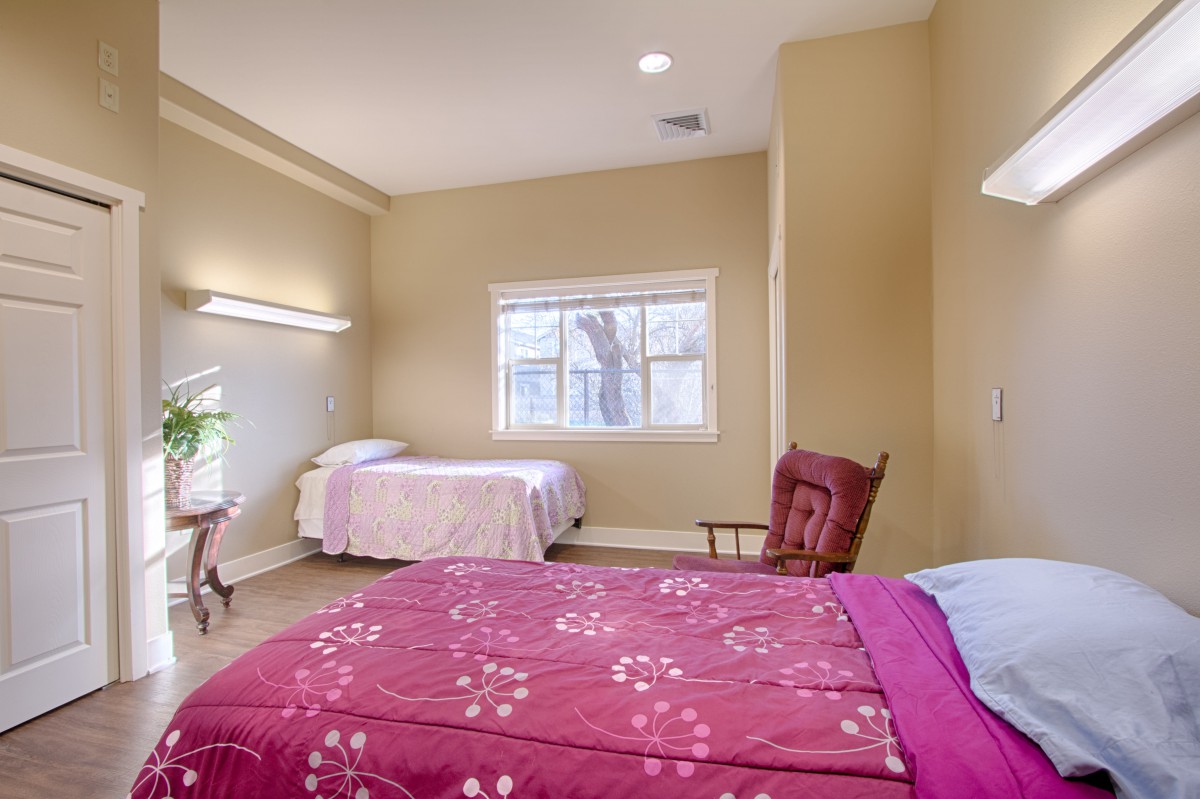 A cozy bedroom with two beds, a window, and a rocking chair.