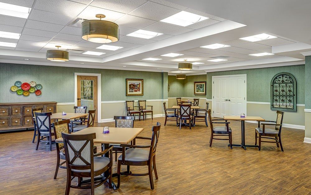 A spacious dining room with neatly arranged tables and chairs, soft lighting, and a wooden floor.