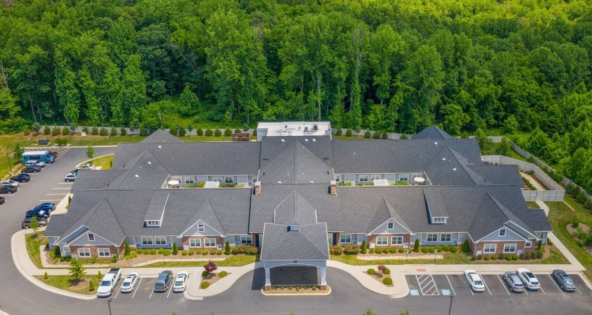 Aerial view of a large building with a parking lot, surrounded by trees.