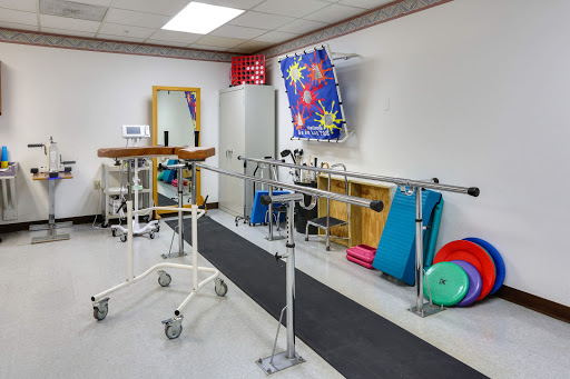 A well-equipped physical therapy room featuring balance bars, exercise mats, and a walking track to aid rehabilitation.
