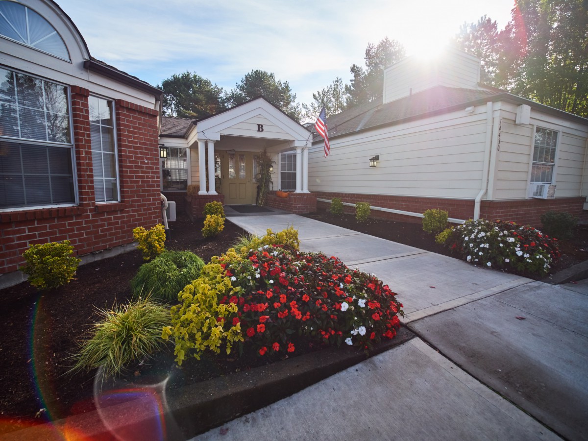 A beautifully landscaped entrance with bright flowers lining the pathway to a building.
