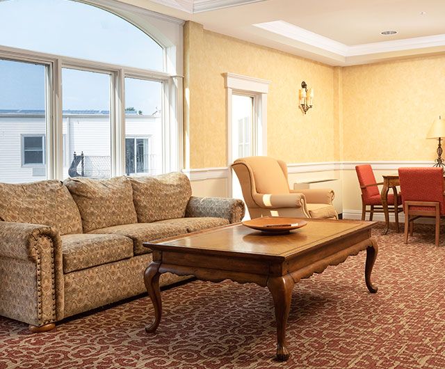 A spacious living room with a classic sofa, armchair, and wooden coffee table, featuring a connected dining area.